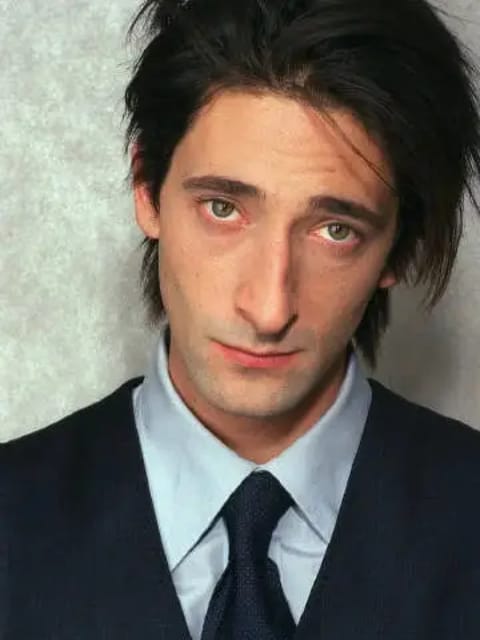 Portrait d'Adrien Brody aux cheveux noirs texturés en désordre. Il porte un costume noir associé à une chemise bleu clair et une cravate noire. Modèle pour l'échange de visage d'image.