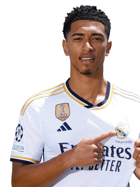 Portrait de Jude Bellingham avec une coupe afro courte noire, portant un maillot domicile blanc du Real Madrid. Il a l'un de ses index pointé vers le logo de Madrid, sur un fond blanc uni.