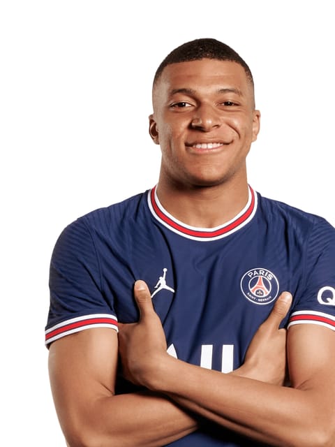Portrait de Kylian Mbappé à la coupe courte buzz, portant le maillot bleu domicile du Paris Saint-Germain. il a les bras croisés et sourit à la caméra sur un fond blanc uni.