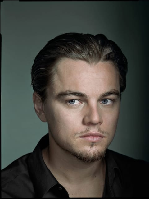Portrait de Leonardo Dicaprio au dos lisse en chemise noire, posant dans un studio faiblement éclairé sur fond vert, regardant hors caméra avec une expression calme. Modèle pour l'échange de visage d'image.