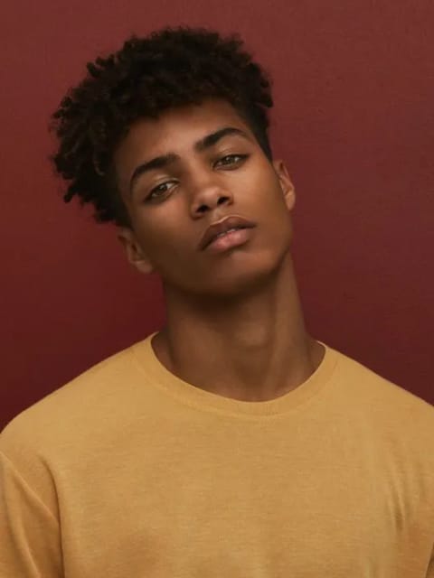Portrait d'un homme à l'afro noir et à l'expression calme, portant un haut jaune à col rond, penchant la tête sur le côté. Modèle pour l'échange de visage d'image.
