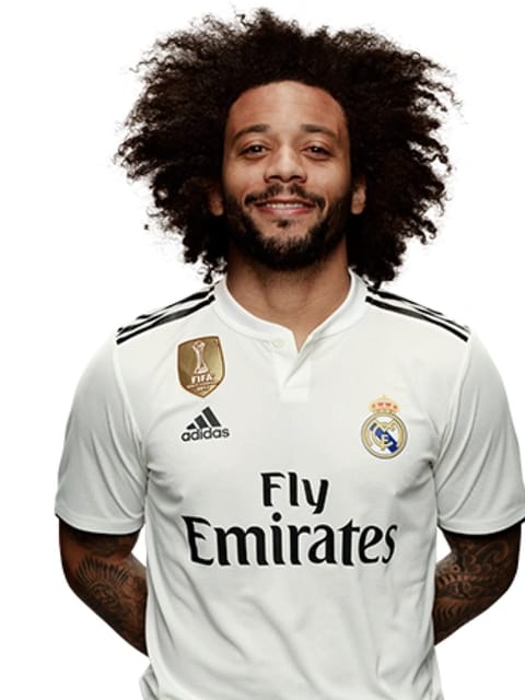 Portrait de Marcelo Vieira avec une grande coupe afro noire et une barbe, portant un maillot blanc domicile du Real Madrid, sur un fond blanc uni, souriant à la caméra.