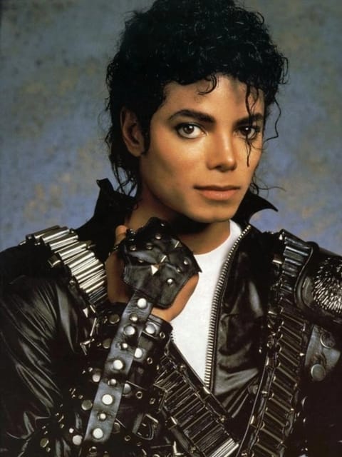 Portrait en studio de Michael Jackson avec ses cheveux noirs bouclés et volumineux. Il porte une veste en cuir noire ornée de clous argentés et de lanières métalliques, un maillot de corps blanc à col rond et le fond est un doux dégradé de teintes bleu clair et jaune pâle. Modèle pour l'échange de visage d'image.