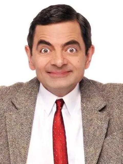 Portrait de M. Bean aux cheveux gominés sur le côté avec une expression exagérée, portant un blazer kaki sur une chemise blanche à col et une cravate rouge. Ses bras s'ouvrent, sur un fond blanc uni.