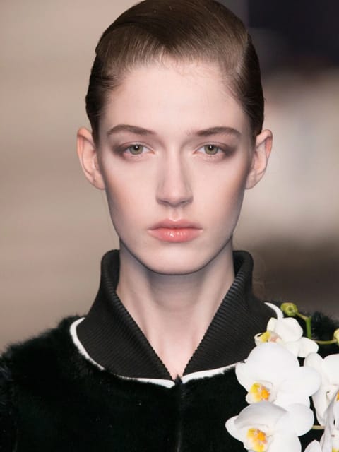 Portrait d'un mannequin aux cheveux lisses tirés en arrière défilant sur le podium, vêtu d'une tenue noire ornée d'une orchidée blanche. Modèle pour l'échange de visage d'image.