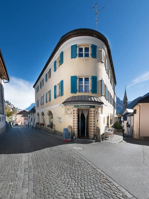 Charmant bâtiment historique aux volets bleus situé au coin d'une rue pavée d'une ville alpine, avec vue sur les montagnes. Modèle pour le filtre Stranger Things.