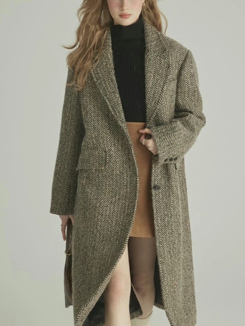 En kvinne i en lang grå frakk og svart turtleneck, med brune sko, modell for AI-klærbytte.