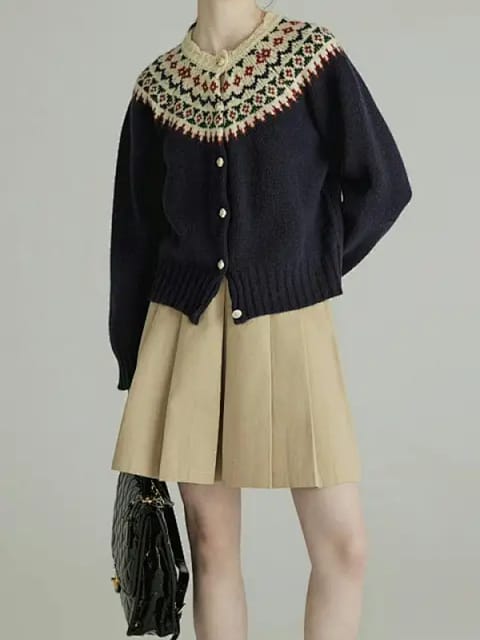 En kvinne i en marine strikket cardigan med mønstret krage, et beige plissert skjørt og svarte sko, modell for AI-klærbytte.