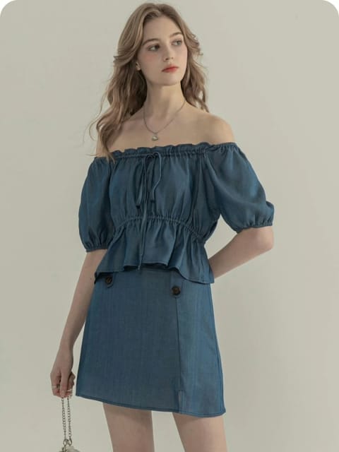 En kvinne i en off-shoulder blå topp og matchende skjørt, med en liten grå veske, modell for AI-klærbytte.